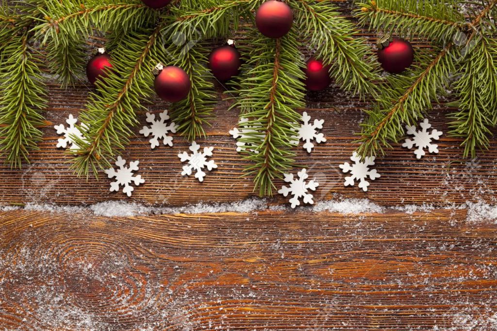 Branch of Christmas tree, red baubles and snowflakes on wooden background